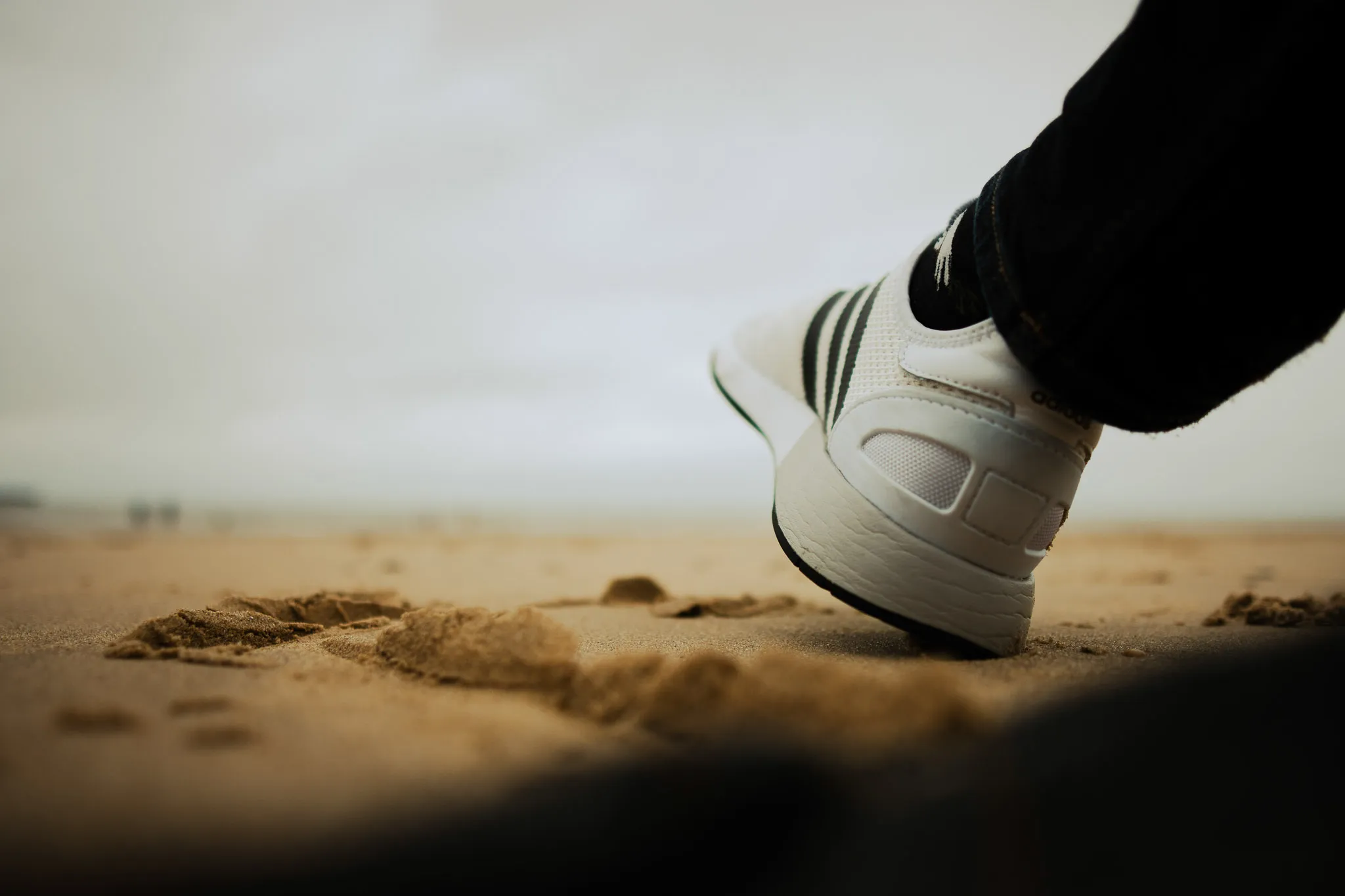 in-focus foot/trainer raised slightly above a very sandy beach.
