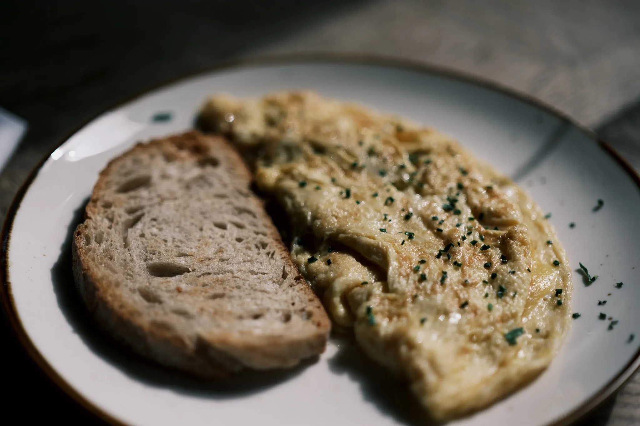 folded ham and cheese omelette with the ham concealed and some green herbs sprinkled on top, next to a slice of toasted sourdough bread served on a white plate