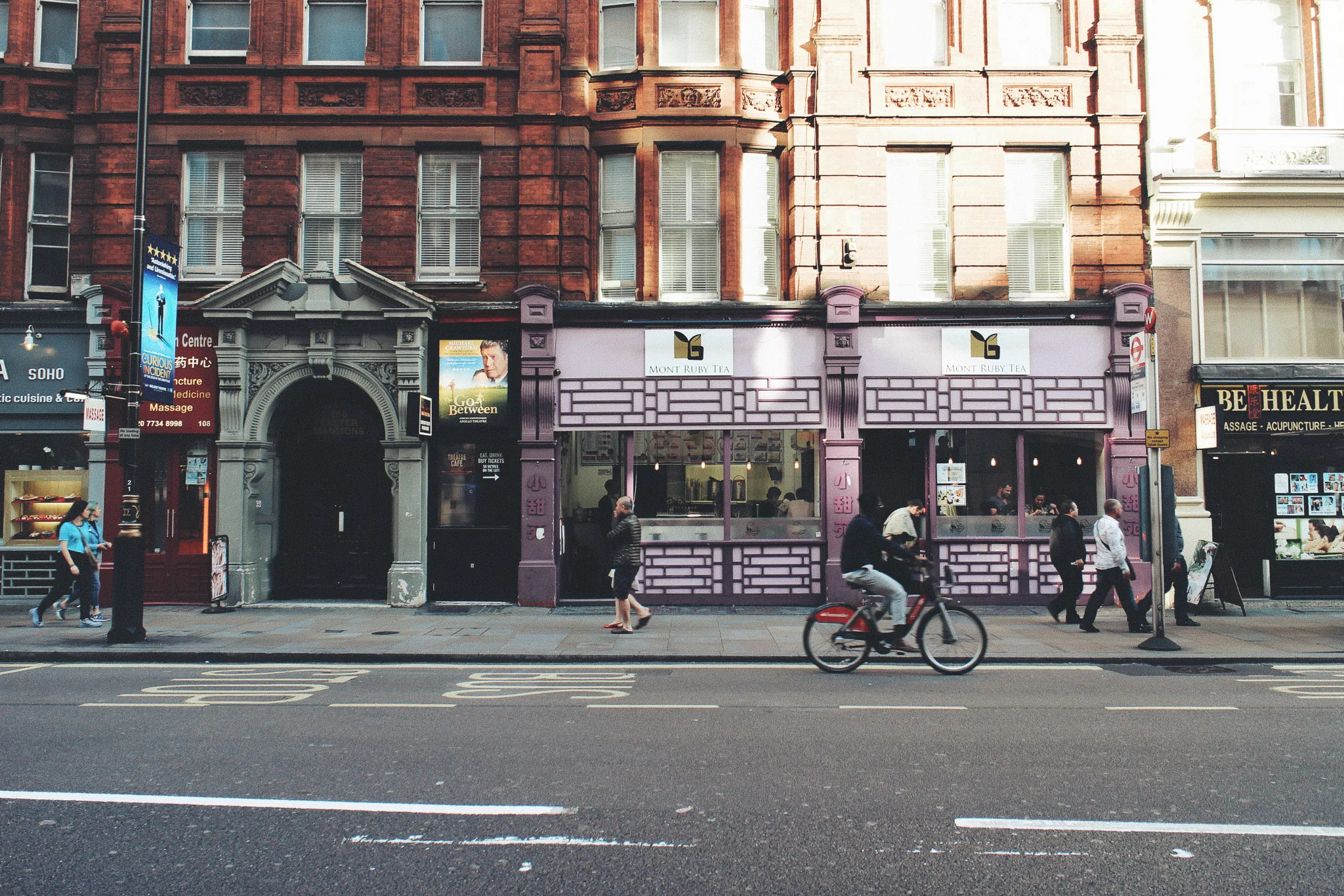 street in Soho, London in the early evening with few people walking on the pavement and one man cycling